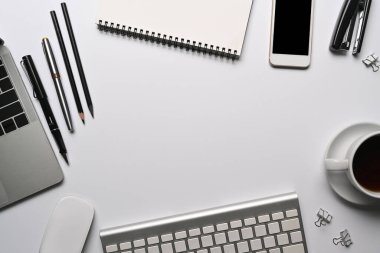 Dizüstü bilgisayarı, cep telefonu ve malzemeleri olan beyaz ofis masası..