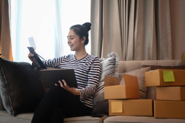 Küçük işletme girişimcisi bilgisayardaki siparişleri kontrol ediyor ve evdeki müşterilere paket hazırlıyor.