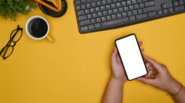 Sarı arka planda akıllı telefon kullanan üst görüşlü adam.