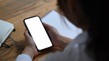 Beyaz ekranlı akıllı telefonu tutan genç bir kadının omuz üstü görüntüsü..