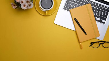 Dizüstü bilgisayarı, bardakları, not defteri ve kahve fincanı ile üst görünümde şık çalışma alanı.