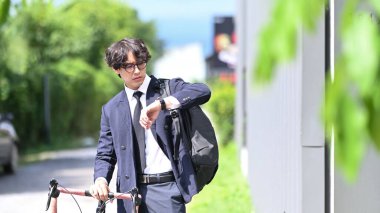 Asyalı işadamı kol saatini kontrol ediyor ve şehir sokaklarında bisikletle yürüyor..