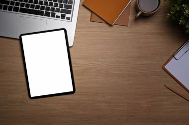 Üst görünüm dijital tablet, dizüstü bilgisayar, defter ve ev bitkisi ahşap masa üzerinde.