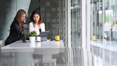 İki başarılı iş kadını modern ofiste proje stratejisini tartışıyor.