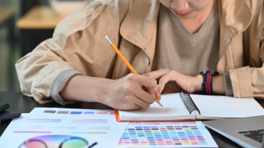 Kırpılmış çekim genç bayan yaratıcı tasarımcı Not defterine not alıyor.