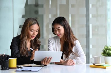 Çekici bir iş kadını dijital tablet kullanarak iş arkadaşıyla bilgi tartışır..