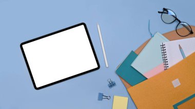 Üst görünüm dijital tablet, not defterleri, bardaklar ve kahve fincanı mavi arkaplanda.