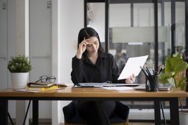 Hüsrana uğramış iş kadını ofiste otururken raporları kontrol ediyor.