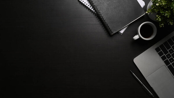 Flat lay modern workspace with computer laptop, coffee cup and book on black table.
