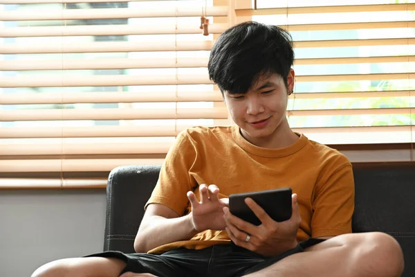 Genç adam rahat bir koltukta oturup dijital tabletle internette sörf yapıyor..