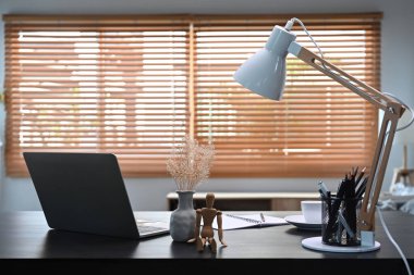 Computer laptop, supplies and white lamp on black wooden table in home office.