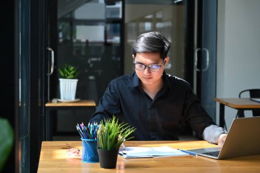 Genç iş adamı dizüstü bilgisayarla çalışıyor ve iş belgelerini analiz ediyor..
