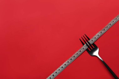 Fork with measuring tape on red background with copy space for text. Loss weight and healthy diet concept.