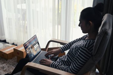 Genç bir kadın evdeki dizüstü bilgisayardan paket teslimatını kontrol ediyor. Çevrimiçi alışveriş kavramı.