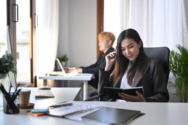 Asyalı iş kadını rahat bir ofis koltuğunda oturup kitap okuyor..