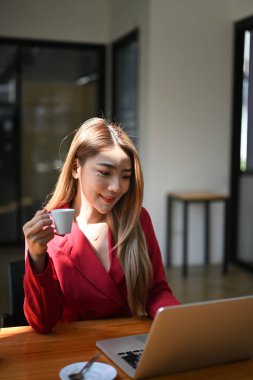 Kahve içen ve dizüstü bilgisayardaki e-postaları kontrol eden düşünceli bir iş kadını..