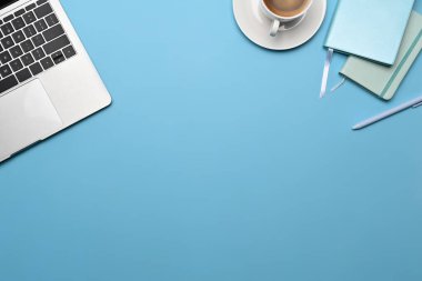 Top view laptop computer, cup of coffee and notebook on blue background.