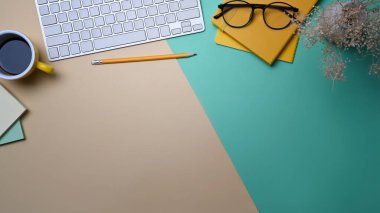 Stylish workspace with notebook, coffee cup and keyboard on colorful background.