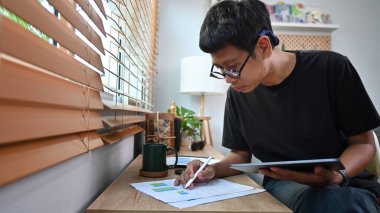 Genç Asyalı adam dijital tabletteki borsa verilerini kontrol ediyor.