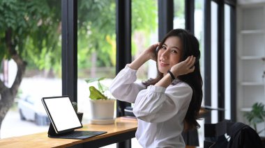 Kablosuz kulaklık takan ve bilgisayar tableti kullanan neşeli genç bir kadın..