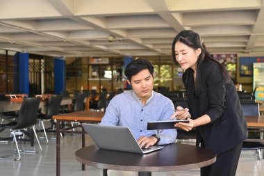 İki iş adamı dizüstü bilgisayar kullanıyor ve ofiste proje başlatma fikirlerini tartışıyorlar.