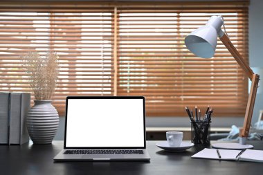 Front view computer laptop with blank screen on black wooden table in home office.