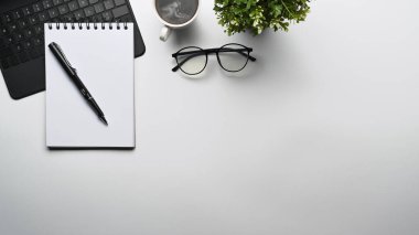 Beyaz masa üzerinde üst görünüm not defteri, gözlük, ev bitkisi ve dizüstü bilgisayar.