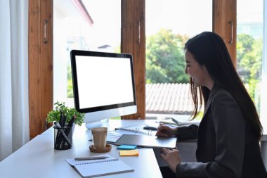 Yan görünüş: Modern iş yerinde bilgisayarla çalışan güzel iş kadını.