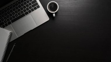 Dizüstü bilgisayar, kahve fincanı ve siyah masanın üzerindeki not defteri..