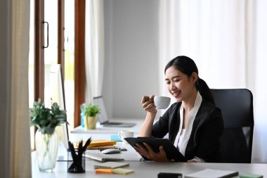 Kahve içen ve dijital tabletten haber okuyan memnun iş kadını..