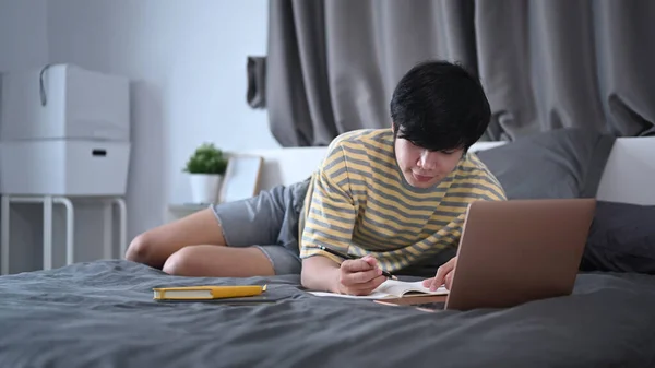 Młody Człowiek Leżący Łóżku Pracujący Lub Studiujący Online Laptopem — Zdjęcie stockowe