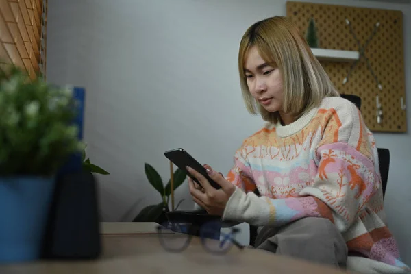 Uśmiechnięta Azjatka Korzystająca Smartfona Siedząc Swoim Biurze — Zdjęcie stockowe