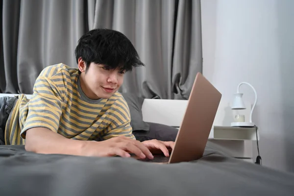 Młody Człowiek Leżący Łóżku Przeglądający Internet Laptopem — Zdjęcie stockowe