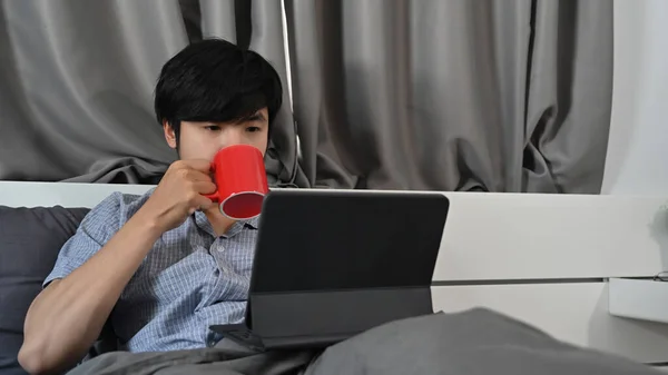 Азиатский Человек Пьющий Кофе Время Использования Компьютера Планшет Кровати Утром — стоковое фото