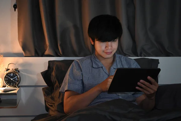 Młody Człowiek Korzystający Tabletu Cyfrowego Podczas Siedzenia Łóżku Nocy — Zdjęcie stockowe