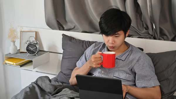 Młody Azjata Pijący Kawę Korzystający Tabletu Łóżku — Zdjęcie stockowe