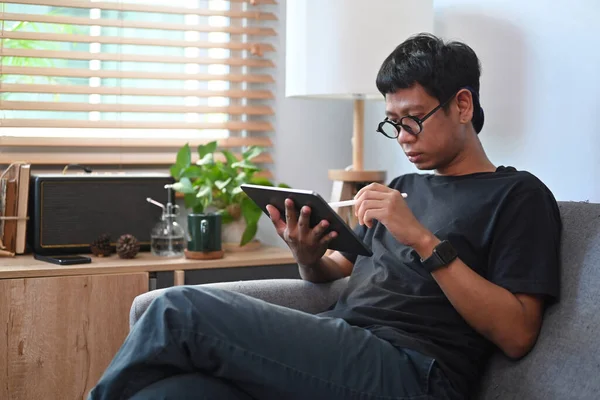 Νεαρός Ασιάτης Κάθεται Στον Καναπέ Και Χρησιμοποιεί Ψηφιακή Ταμπλέτα — Φωτογραφία Αρχείου
