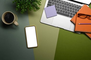Akıllı telefon, dizüstü bilgisayar, kahve fincanı ve yeşil arka plandaki defter..