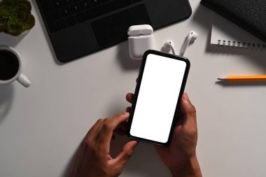 Yukarıda beyaz masada akıllı telefonu tutan genç bir adam var..