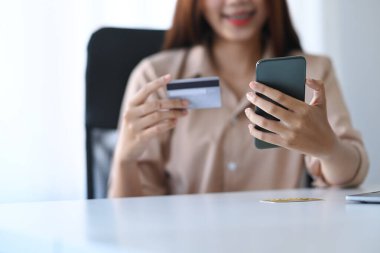 Gülümseyen Asyalı kadın akıllı telefonuyla online bankacılık veya alışveriş yapıyor..