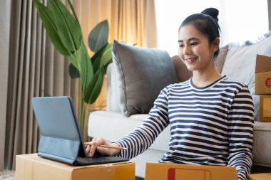 Gülümseyen genç Asyalı kadın bilgisayar tabletinden online siparişi kontrol ediyor.
