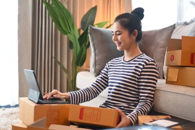 Küçük işletme KOBİ kavramı başlat. Genç bir kadın internetten siparişleri kontrol ediyor ve teslimat için paket kutusu hazırlıyor..