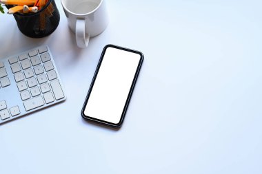 Üst görünüm akıllı telefon, kahve fincanı ve kalem tutacağı beyaz ofis masasında..