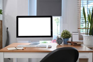 Bilgisayarı, çalar saati, kitabı, kahve fincanı ve bitkisi olan ofis masası.. 