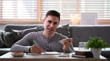 Gülümseyen adam deftere notlar alıyor ve cep telefonuyla konuşuyor..