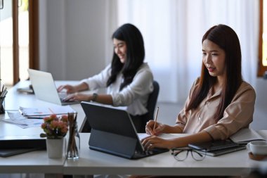 Meslektaşımla ofiste otururken bilgisayar tabletleriyle çalışan çekici bir iş kadını..