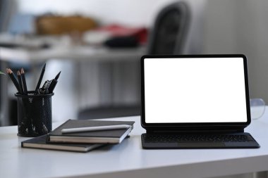Beyaz masadaki kablosuz klavye, defter ve kalem tutacağı olan dijital tablo..