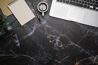 Laptop bilgisayarı, not defteri ve mermer arka planda kahve fincanı olan şık çalışma alanı.