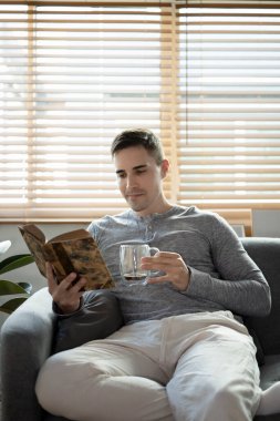 Yakışıklı bir adamın portresi. Kahve içiyor ve rahat koltukta kitap okuyor..