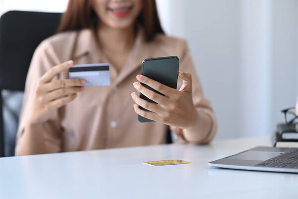 Smiling young woman holding credit card and smart phone for payment online.